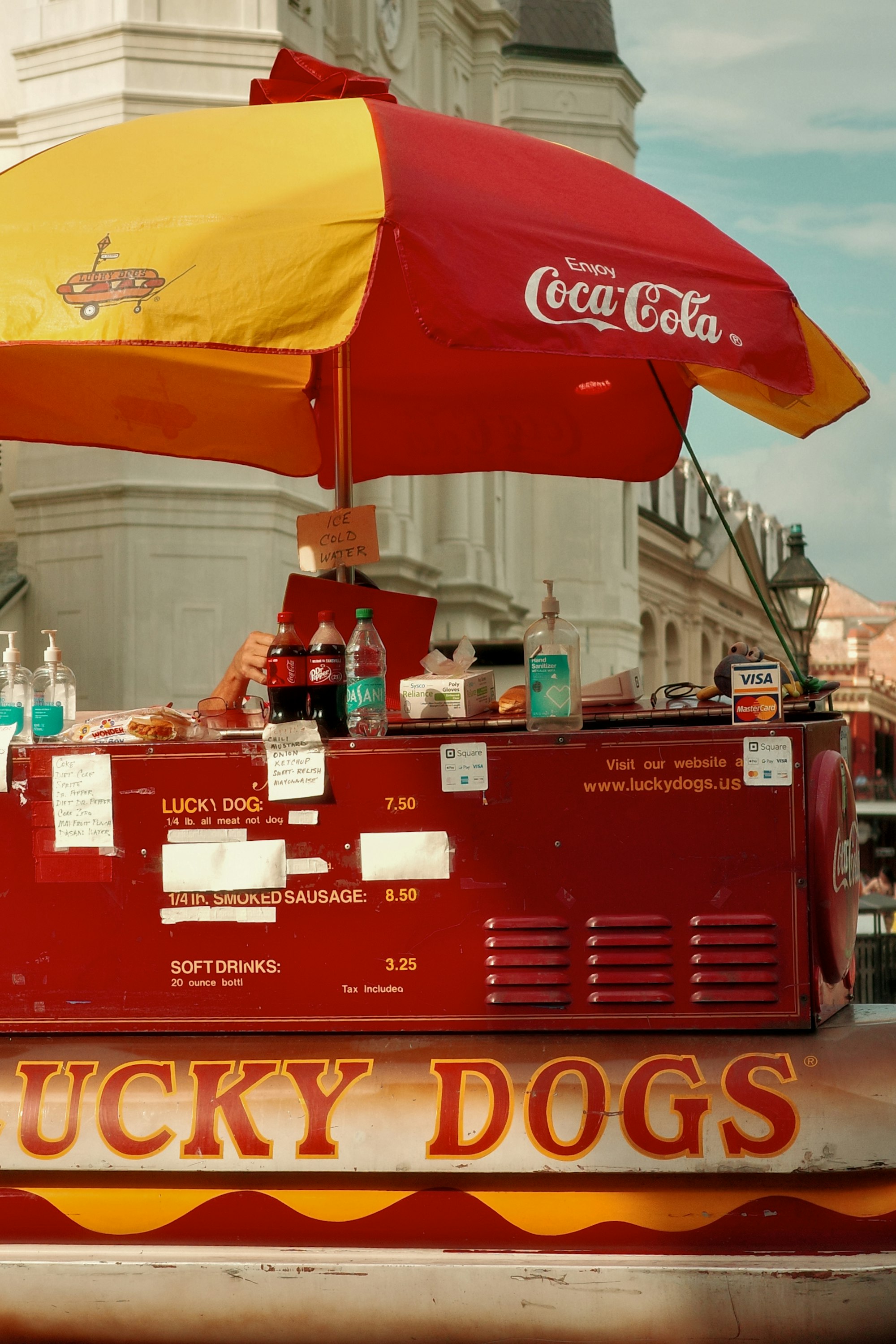 A red and yellow hot dog cart with an umbrella set up on a city street